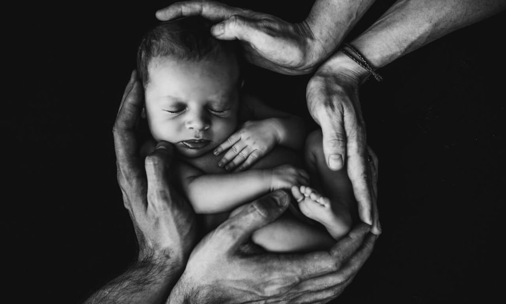 Newborn baby held in the hands of it's 2 parents (black and white)