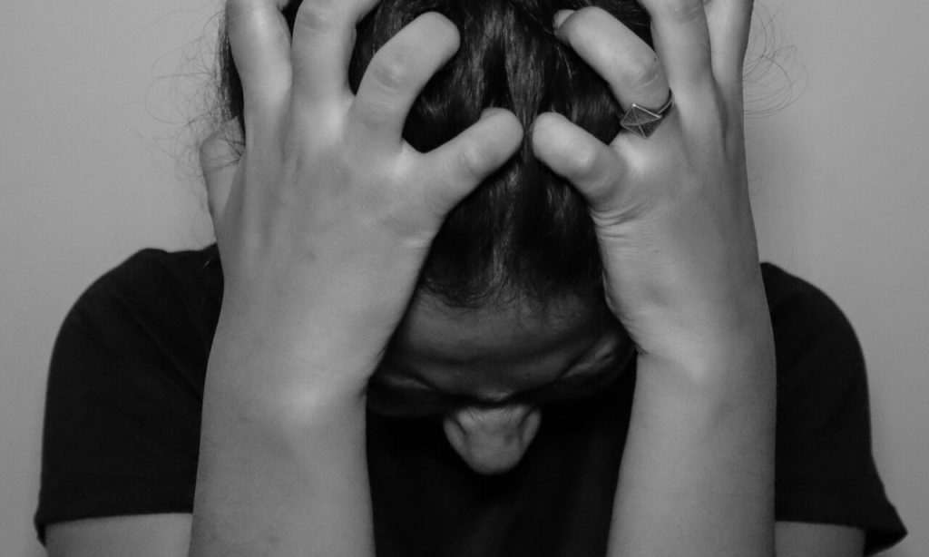 Woman with hands in her hair, head down, stressed out