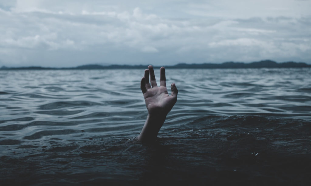 Hand reaching out from under the water of a lake for help.
