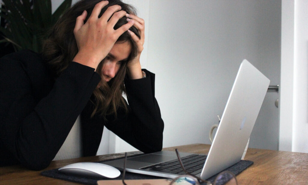 Woman leaning over laptop with her hands on her head, stressed out
