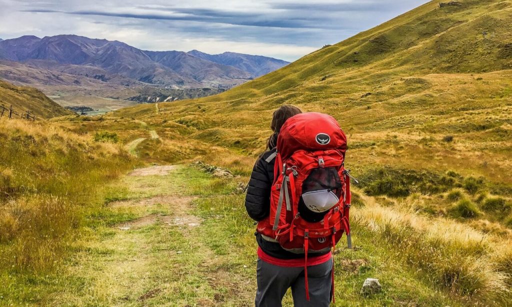 Picture of Laura hiking in mountains with red backpack, looking off into the distance